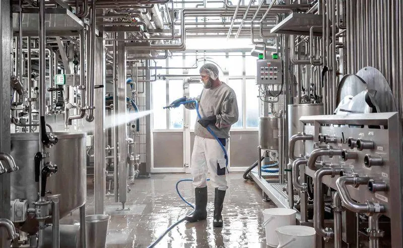 Opérateur en tenue de protection nettoyant à l’eau des équipements en inox
